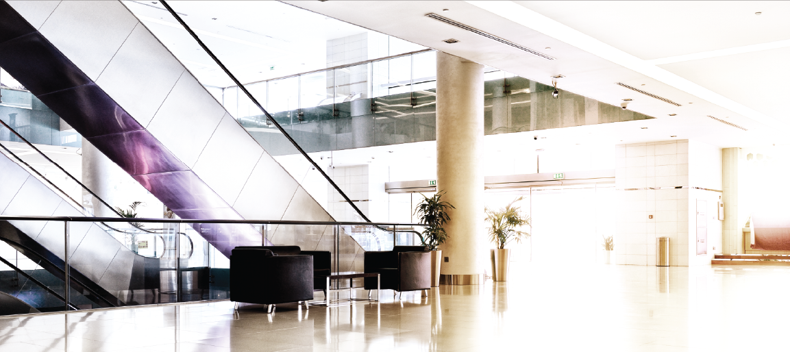 Bright modern office lobby with escalator, glass railings and lounge seating, contemporary corporate building interior and reception area.