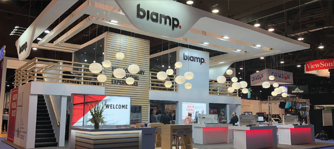 Biamp trade show booth display at pro AV expo, featuring modern lighting, welcome desk, and audio-visual solutions demo area.