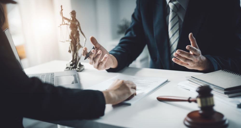Lawyer consultation at office desk with legal documents, gavel, and Lady Justice statue, attorney meeting and legal services concept