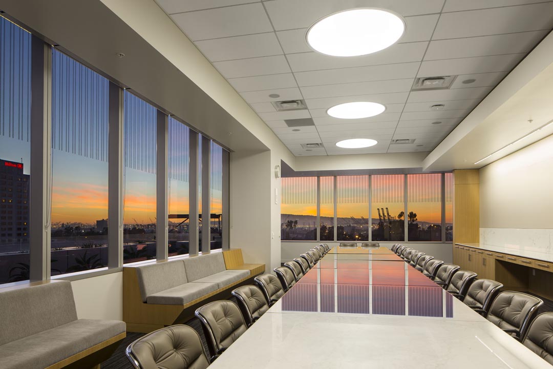 Modern boardroom conference room with long table, leather chairs, and sunset city view through large windows