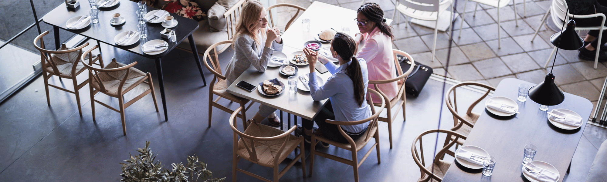 Overhead view of friends dining at modern restaurant, group conversation at table with shared plates, casual lunch meeting in cafe.