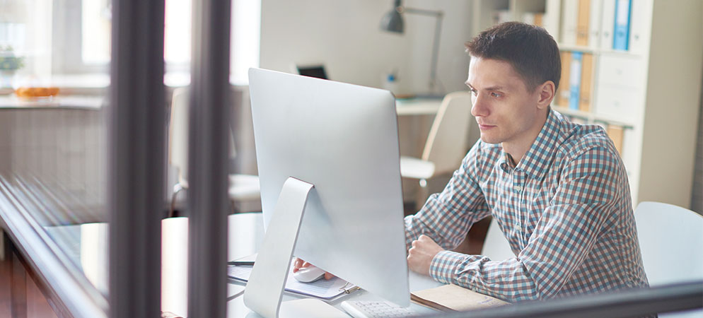 Young professional working at desktop computer in modern office, focused on tasks in a bright workspace with shelves and files