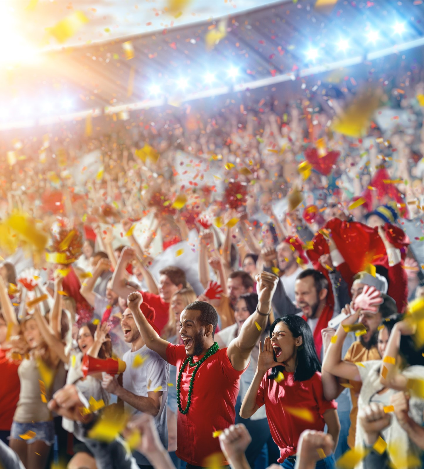 Cheering stadium crowd celebrating with confetti and raised arms, energetic sports fans at live game or concert in packed arena.