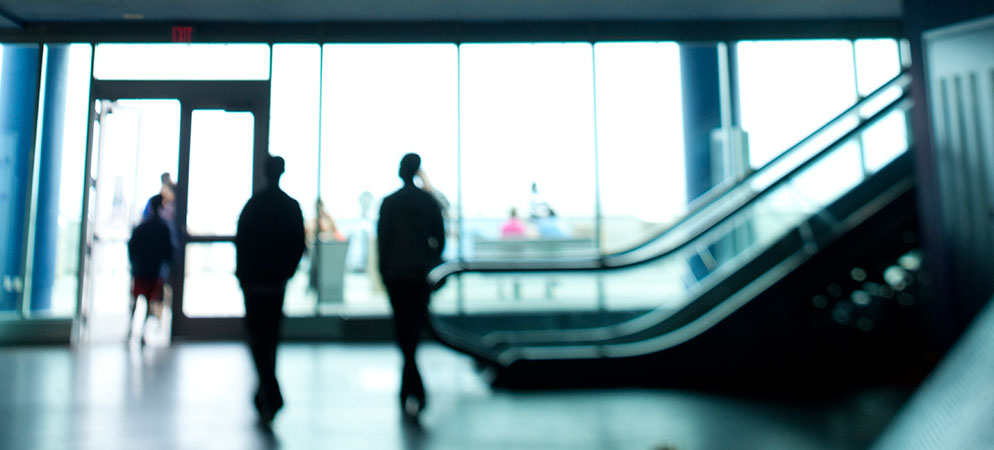 Blurred people walking in modern building lobby with escalator and glass entrance, corporate office interior and business travel concept
