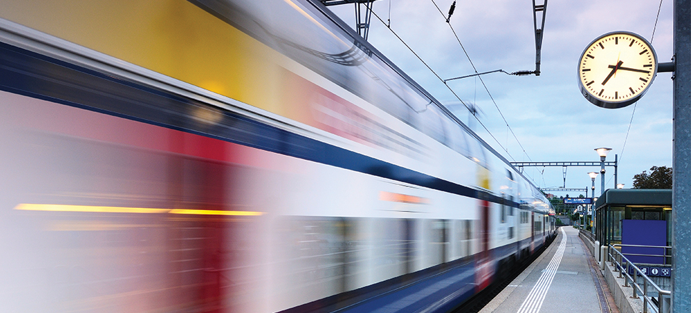 Blurred train speeding through station platform with large clock, capturing fast public transit commute and railway travel at dusk