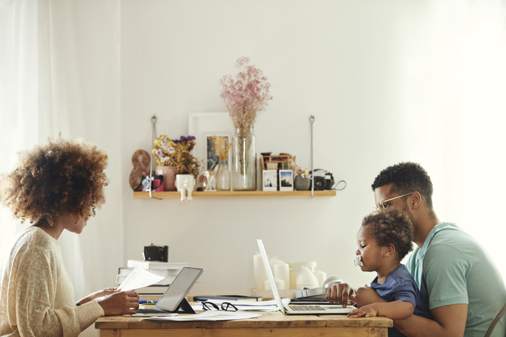 Family working and studying at home office table with laptops and tablet, parents and child remote work and online learning in bright room.