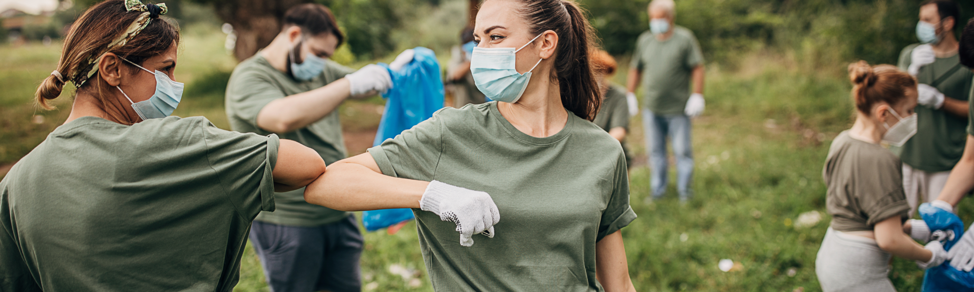 Volunteers wearing masks and gloves during park cleanup, elbow bump greeting while collecting trash, community service and environmental action.