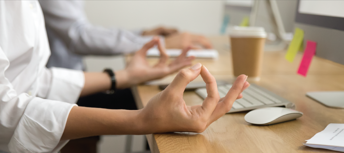 Office workers meditating at desk with hands in yoga pose, promoting workplace wellness, stress relief, and mindful productivity break