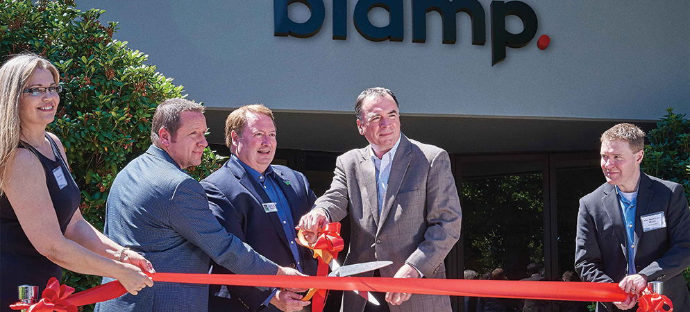 Biamp headquarters ribbon-cutting ceremony outside office building, executives cutting red ribbon at company event and grand opening.