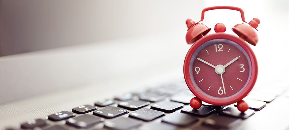 Red alarm clock on computer keyboard, symbolizing deadlines, time management, productivity, and work schedule planning in office setting