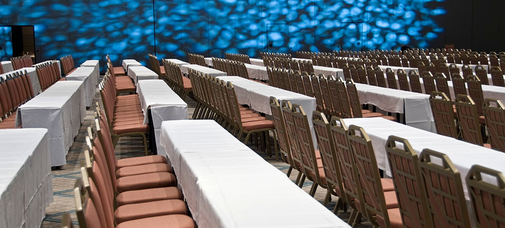Conference ballroom setup with long tables and rows of chairs, meeting room seating arranged for seminar or corporate training event
