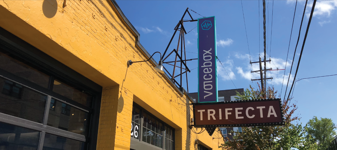 Trifecta Voicebox venue exterior with yellow brick facade and hanging sign on sunny day, urban storefront and event space entrance