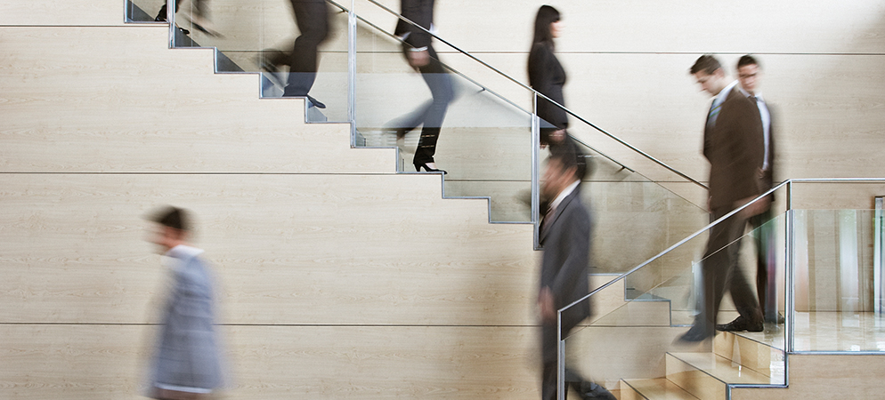 Blurred business people walking up office staircase, modern corporate building interior, busy workplace movement and commuting concept.