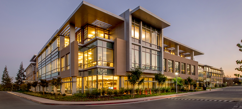 Modern glass office building exterior at dusk with illuminated windows, contemporary corporate headquarters and business campus architecture.