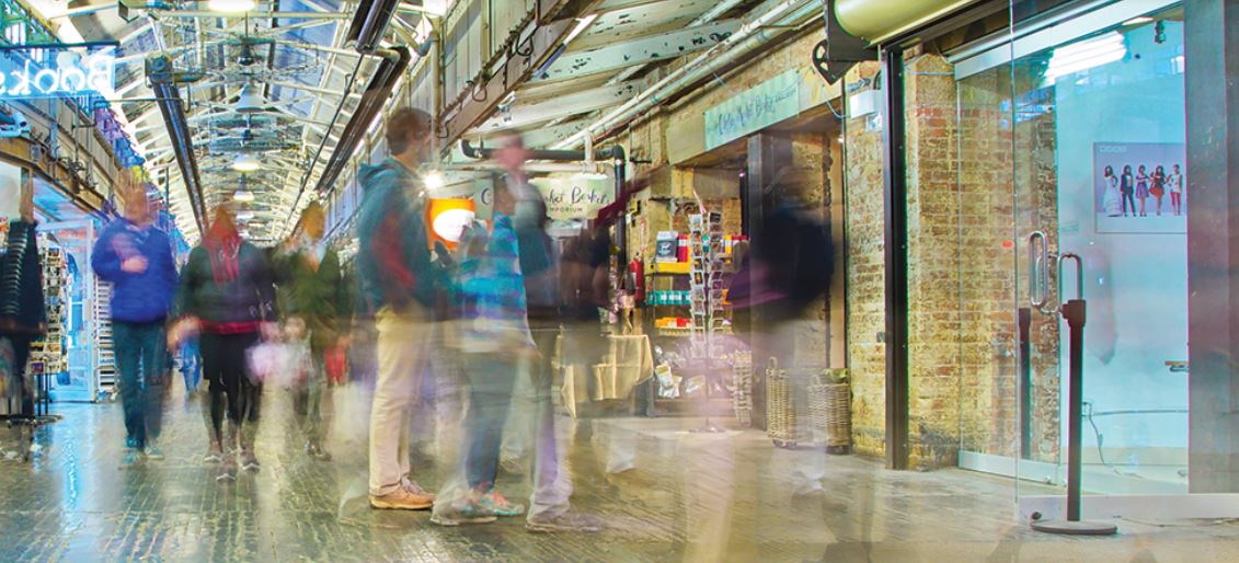Busy indoor shopping arcade with blurred pedestrians, retail corridor scene showing customer foot traffic and storefronts
