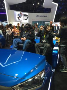 Image of people with VR headsets on behind a mocked up car hood.