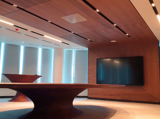 Modern conference room with ceiling tile microphone, wood-paneled walls, large display, and presentation table