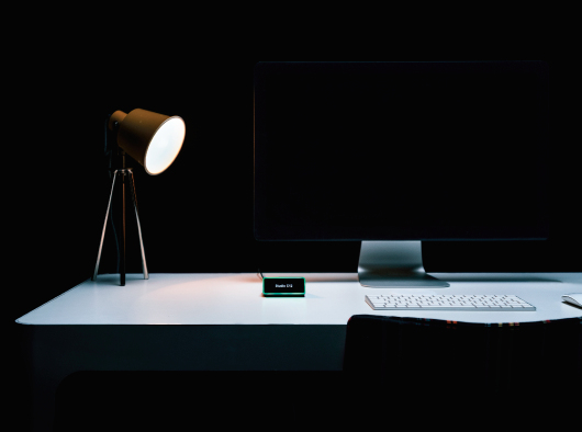 Minimal desk setup with monitor, lamp, and Kleeo smart device on a modern dark workspace desk
