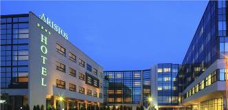 Exterior of the modern, glass-fronted Aristos Hotel at dusk, with illuminated signage and windows.