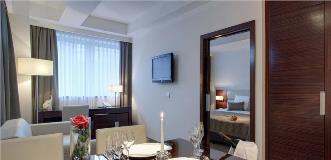 Modern hotel suite with a dining table set for two and a separate bedroom visible through an open wooden sliding door.
