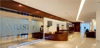 Sleek hotel or office lobby with a polished floor, wood-paneled reception desk, and glass wall labeled “ARISTOS.”