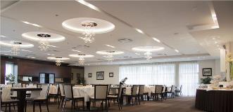 Spacious hotel restaurant with white tablecloths, modern chandeliers, and a server setting tables near large windows.
