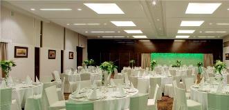 Elegant banquet hall set for an event with round tables, white linens, and green floral centerpieces under modern ceiling lights.