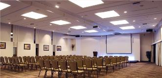 Conference hall set theater-style with rows of chairs facing a large projection screen and podium.