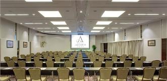 Hotel Aristos conference room arranged classroom-style with rows of tables and chairs facing a projection screen.