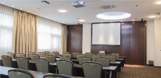 Small conference room with rows of chairs and tables facing a projection screen and ceiling-mounted projector.
