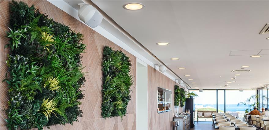 Modern coastal restaurant interior with wall-mounted vertical gardens, sleek lighting and ocean views through large windows.