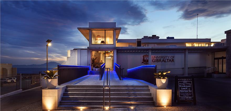 University of Gibraltar building at dusk with illuminated entrance steps and modern architecture overlooking the sea.