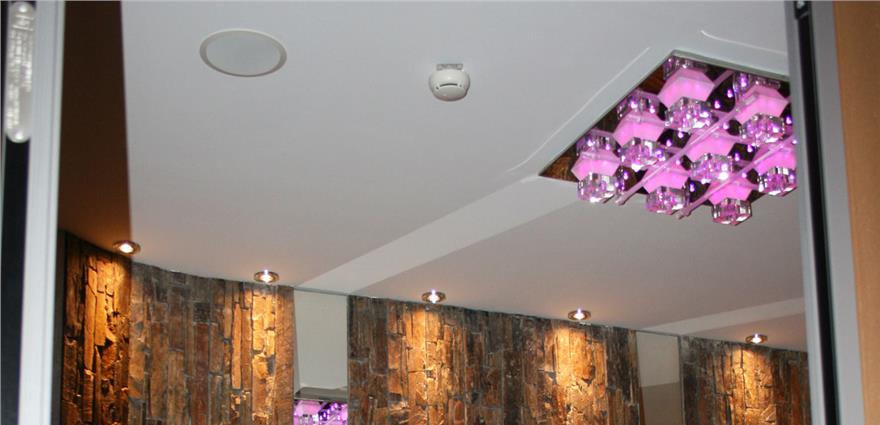Elegant indoor dining area with a purple geometric chandelier, modern lighting, and textured stone wall accents.