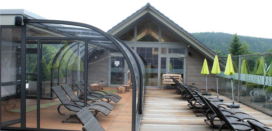 Rooftop terrace with glass-walled lounge, sun loungers, yellow umbrellas, and a mountain backdrop.