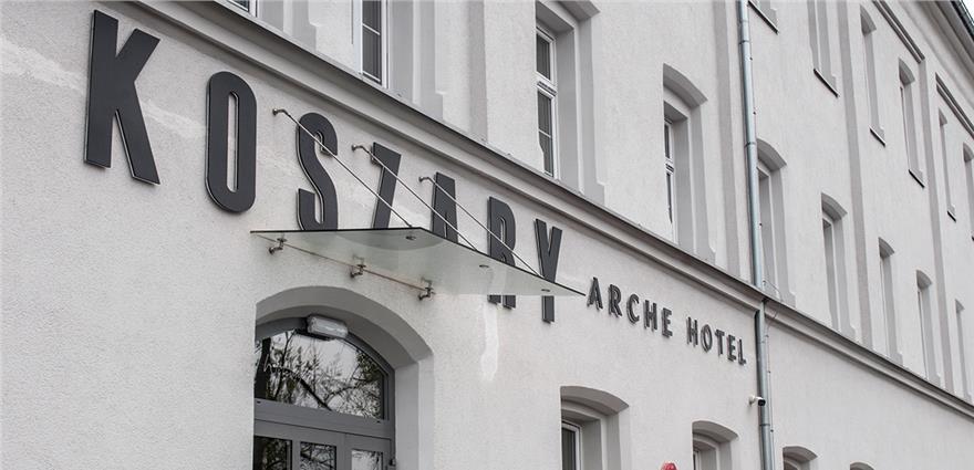 Exterior view of a white brick hotel facade with a large black "KOSTRY" sign and "ARCHE HOTEL" lettering.
