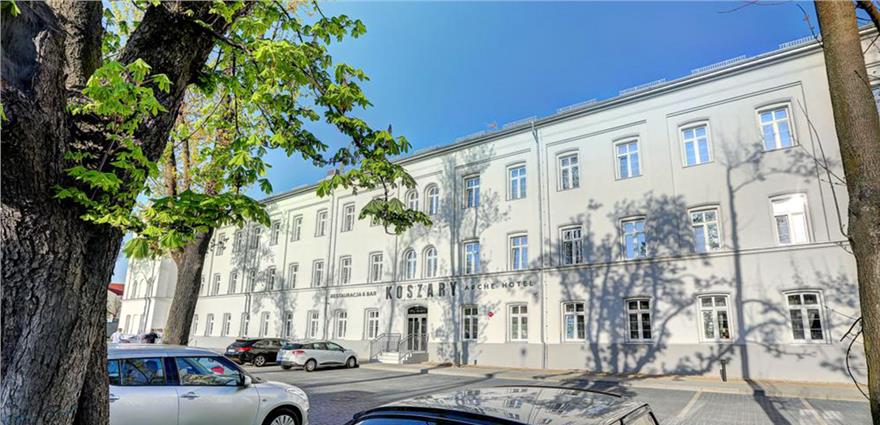 Exterior view of Kostary Arche Hotel, a white multi-story building with arched windows and street-side parked cars.