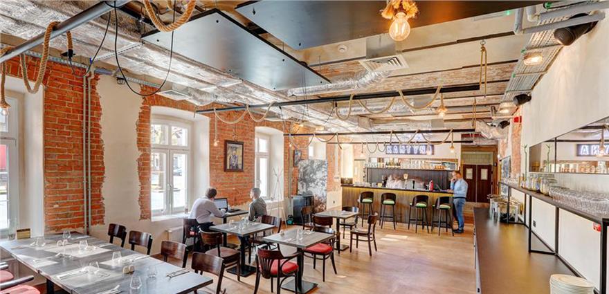 Industrial-style restaurant interior with exposed brick walls, rustic wooden tables, and a long bar.