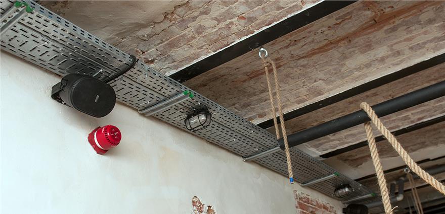 Industrial ceiling with exposed brick, metal cable tray, speaker, and hanging ropes.