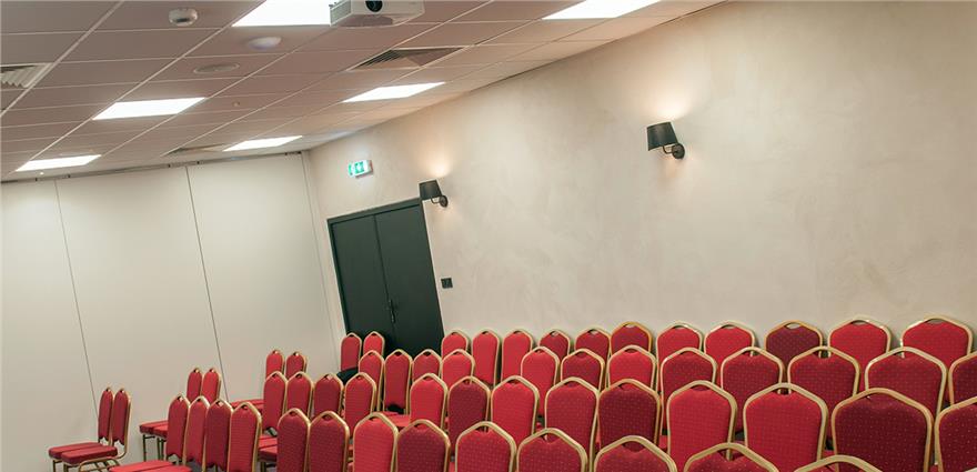 Conference room with rows of red upholstered chairs set for a meeting or presentation.