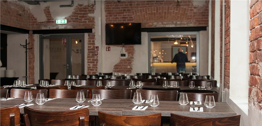 Brick-walled dining room with wooden tables set for dinner and an open kitchen view.