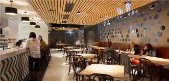 Modern restaurant interior with honeycomb hex wall panels, wooden slat ceiling, and dining tables.