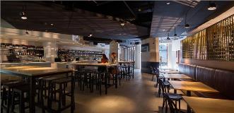 Modern restaurant interior with a long bar, wooden tables, and hexagonal wall panels.