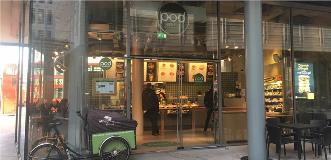 Pod Good Food storefront with glass doors, cafe counter, menu boards, and customers ordering inside.