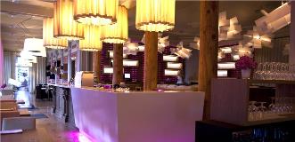 Modern restaurant interior with a long white bar, wooden pillars, warm pendant lights, and purple accent lighting.