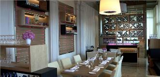 Elegant restaurant interior with a long wooden dining table, wine racks, and pink floral centerpiece.