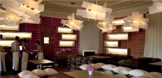 Contemporary lounge bar with white geometric pendant lights, pink backlit walls, and cushioned seating.