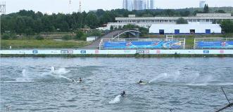 Jet ski riders racing on a water sports course with grandstands, banners and forest backdrop.