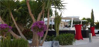 Chic outdoor lounge bar with lush landscaped garden, white canopy seating and tall red cocktail tables.