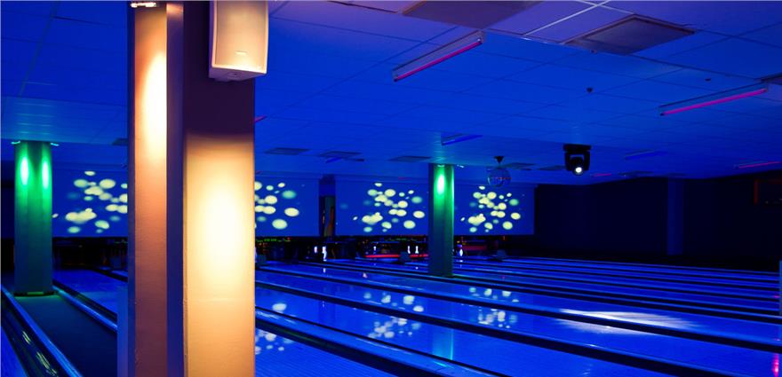 Glow-in-the-dark bowling alley with blue-lit lanes and colorful projections on the back wall.