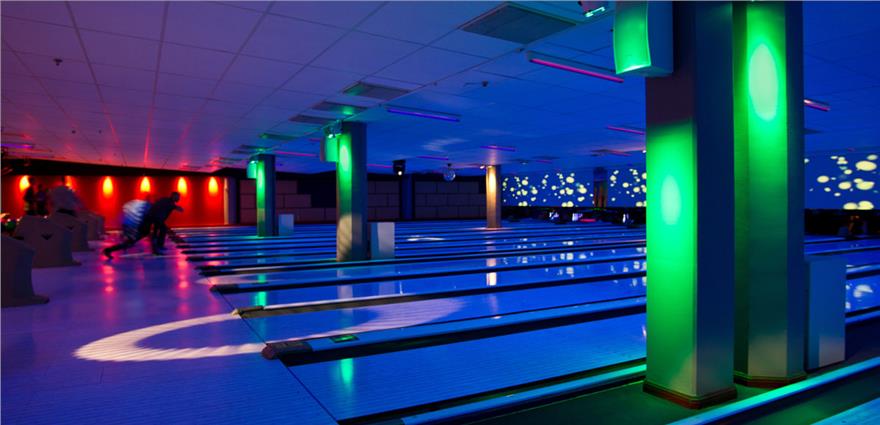 Cosmic bowling alley with glowing lanes, colorful lights on pillars, and bowlers at the far end.